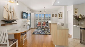 A modern kitchen with a central island, wooden flooring, and a dining area with a table and chairs. - The Pool Resort Kingscliff - One Bed Ocean View (2308) - Holiday Management Co. (Tweed)