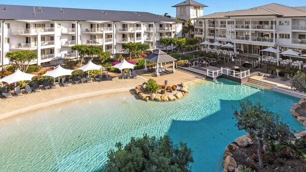 A resort with a large pool, lounge chairs, umbrellas, and a multi-story building with balconies. - The Pool Resort Kingscliff - One Bed Ocean View (2308) - Holiday Management Co. (Tweed)