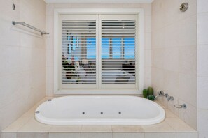 Uma casa de banho moderna com uma banheira grande, uma janela com persianas e um porta-toalhas.