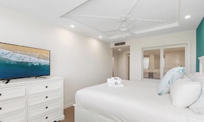 Une chambre à coucher avec un lit, un téléviseur, un ventilateur de plafond et une fenêtre avec des stores.