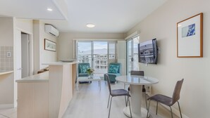 Una cocina moderna con una isla central, un comedor con una mesa redonda y sillas, y un balcón con vistas a edificios.