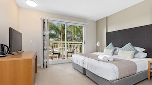 Une chambre avec un lit, un bureau, une télévision et un balcon équipé de chaises.
