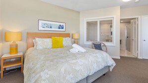 A hotel room with a large bed, two bedside lamps, a ceiling fan, a window with shutters, and a framed picture on the wall.