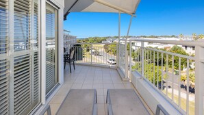 A balcony with two chairs, a table, and a view of a residential area with houses and greenery.
