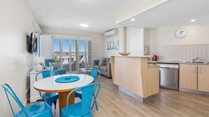 A modern kitchen with a dining area, featuring a central island, blue chairs, and a built-in dishwasher.