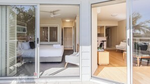 A modern hotel room with a large sliding glass door leading to a balcony, a bed with a white headboard, and a small seating area with a table and chairs. - The Pool Resort Kingscliff - 1 BR Spa Suite (7314) - Holiday Management Co. (Tweed)