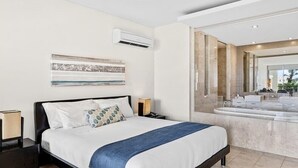 Habitació d'hotel moderna amb un llit gran, una tauleta de nit, aire condicionat fixat a la paret i un bany amb un mirall gran i un lavabo.