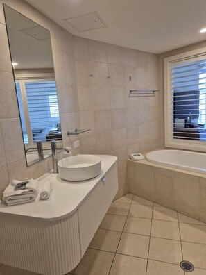 A modern bathroom with a round sink, a mirror, a window, and a bathtub.