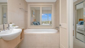 Et moderne badeværelse med et fristående badekar, et toiletbord med vask og et vindue med persienner.