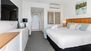 Et moderne hotelværelse med en stor seng, et fladskærms-tv, et minibar og et billede af et tropisk landskab.