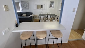 Cocina compacta con una isla central, zona de comedor con sillas y un sofá al fondo.