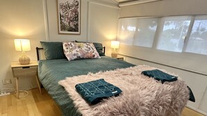 Un dormitorio con una cama grande, dos mesitas de noche con lámparas, una alfombra mullida y una ventana con persianas.