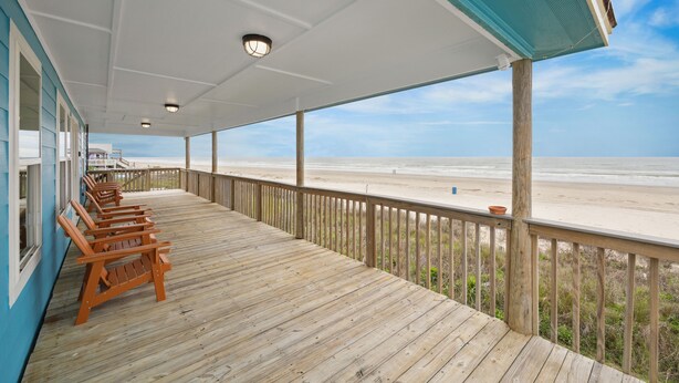 Una terraza de madera con sillas y vistas a la playa.