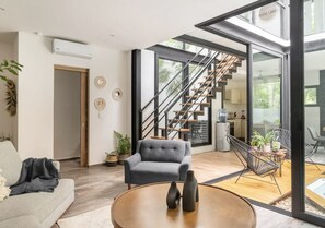 A modern living room with a grey sofa, a round coffee table, and a staircase leading to an upper level.