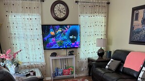 A living room with a leather sofa, a red patterned rug, a television, and a clock on the wall. - Quiet and cozy home away from home I (Bay St. Louis)