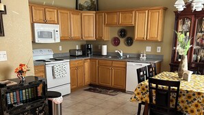 A kitchen with wooden cabinets, a microwave, a stove, and a dining area with a table and chairs. - Quiet and cozy home away from home I (Bay St. Louis)