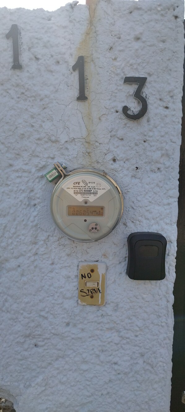 A utility meter with a digital display, a handwritten note, and a black object on a textured wall with numbers 1 and 3 visible. - Casa Alcatraz Querétaro Cerca del Tec de Monterrey (Querétaro)