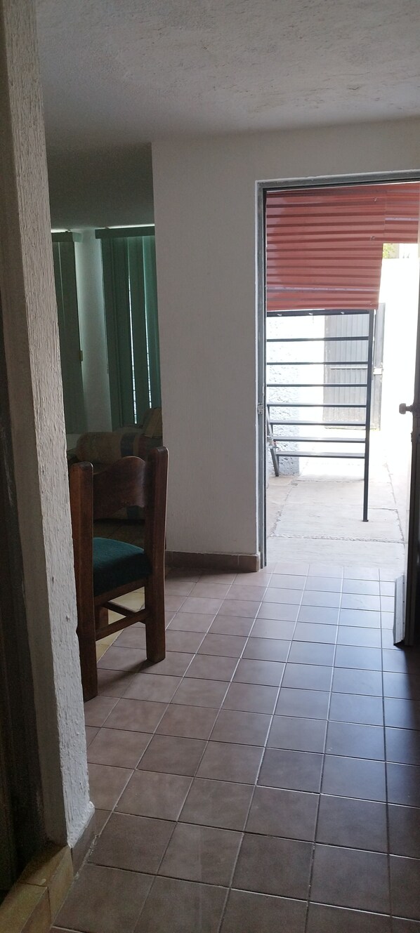 Un pasillo con piso de baldosas, una silla de madera y una puerta que da al exterior.