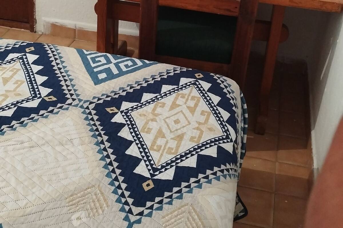 Una habitació amb llit, taula de fusta i cadira.