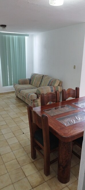 A dining area with a wooden table and chairs, a striped sofa, and a window with blinds. - Casa Alcatraz Querétaro Cerca del Tec de Monterrey (Querétaro)