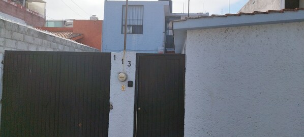 A gated entrance with a white wall and a blue building in the background. - Casa Alcatraz Querétaro Cerca del Tec de Monterrey (Querétaro)