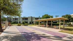 Un patio con mesas para el juego de shuffleboard, asientos exteriores y una zona cubierta.
