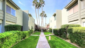 Un sendero bordeado por setos podados y palmeras, que conduce a un edificio de estilo arquitectónico moderno.