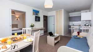 A compact hotel room with a kitchenette, a dining area with breakfast, a bed, and a small workspace. - Appartement au calme, à 15 min de la plage ! (La Rochelle)
