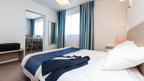 A hotel room with a bed, bedside lamp, curtains, and a desk with a chair. - Appartement au calme, à 15 min de la plage ! (La Rochelle)