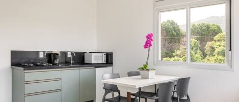 A modern kitchen with a dining area, a view of trees through a window, and a potted orchid on the table.