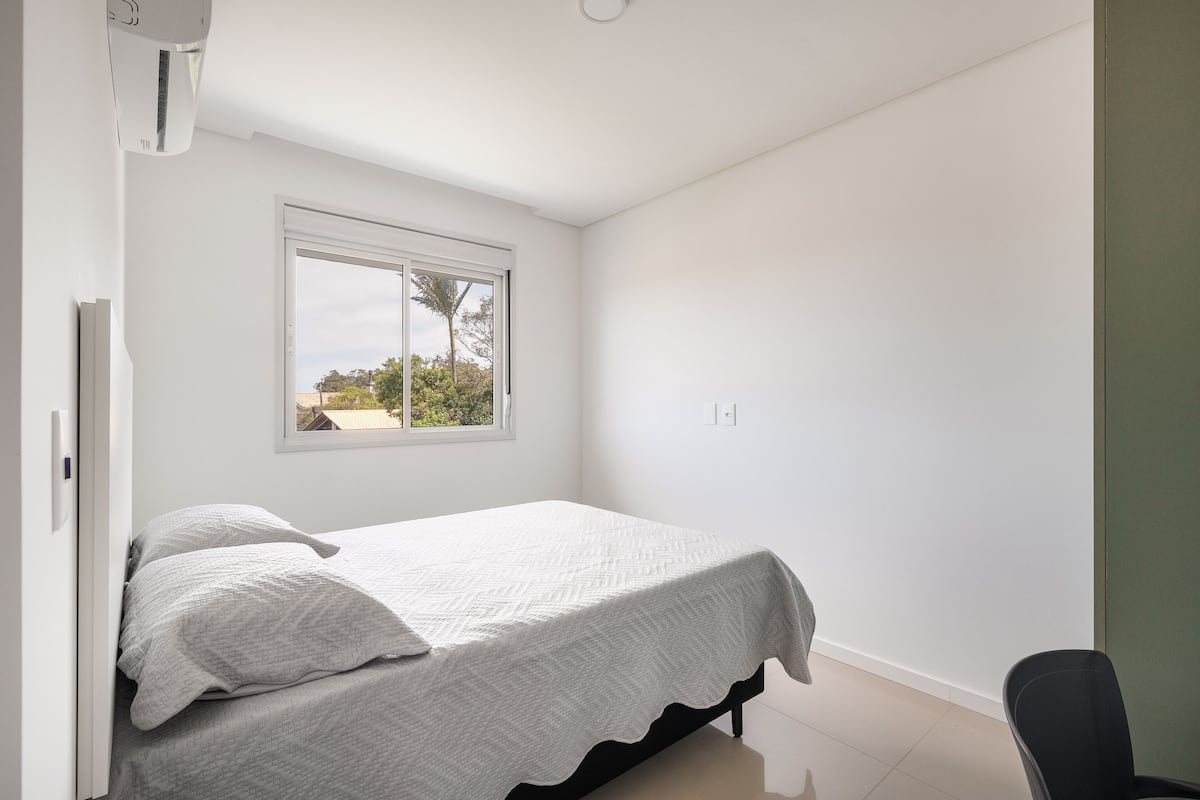 A bedroom with a bed, a window, and a chair.