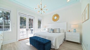 Une chambre à coucher avec un grand lit, un banc bleu, une commode blanche et un miroir en forme de soleil accroché au mur.