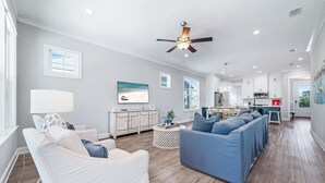 A spacious living room with a white sofa, blue sofa, and a white armchair. There is a ceiling fan, a dining area with a table and chairs, and a kitchen with white cabinets and a red appliance. - Coastal Luxury Beach Escape with Plenty of Room! Pool and Golf Nearby (Orange Beach)