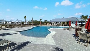 A pool area with lounge chairs and umbrellas, surrounded by a fence and palm trees. - Coastal Luxury Beach Escape with Plenty of Room! Pool and Golf Nearby (Orange Beach)