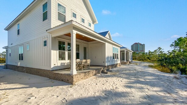 A large, single-story house with a covered porch and a small deck, situated on sandy ground with a clear sky. - Coastal Luxury Beach Escape with Plenty of Room! Pool and Golf Nearby (Orange Beach)