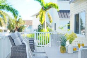 Une terrasse avec des meubles d’extérieur, un ananas, un vase rempli de fleurs et un verre de jus d’orange.
