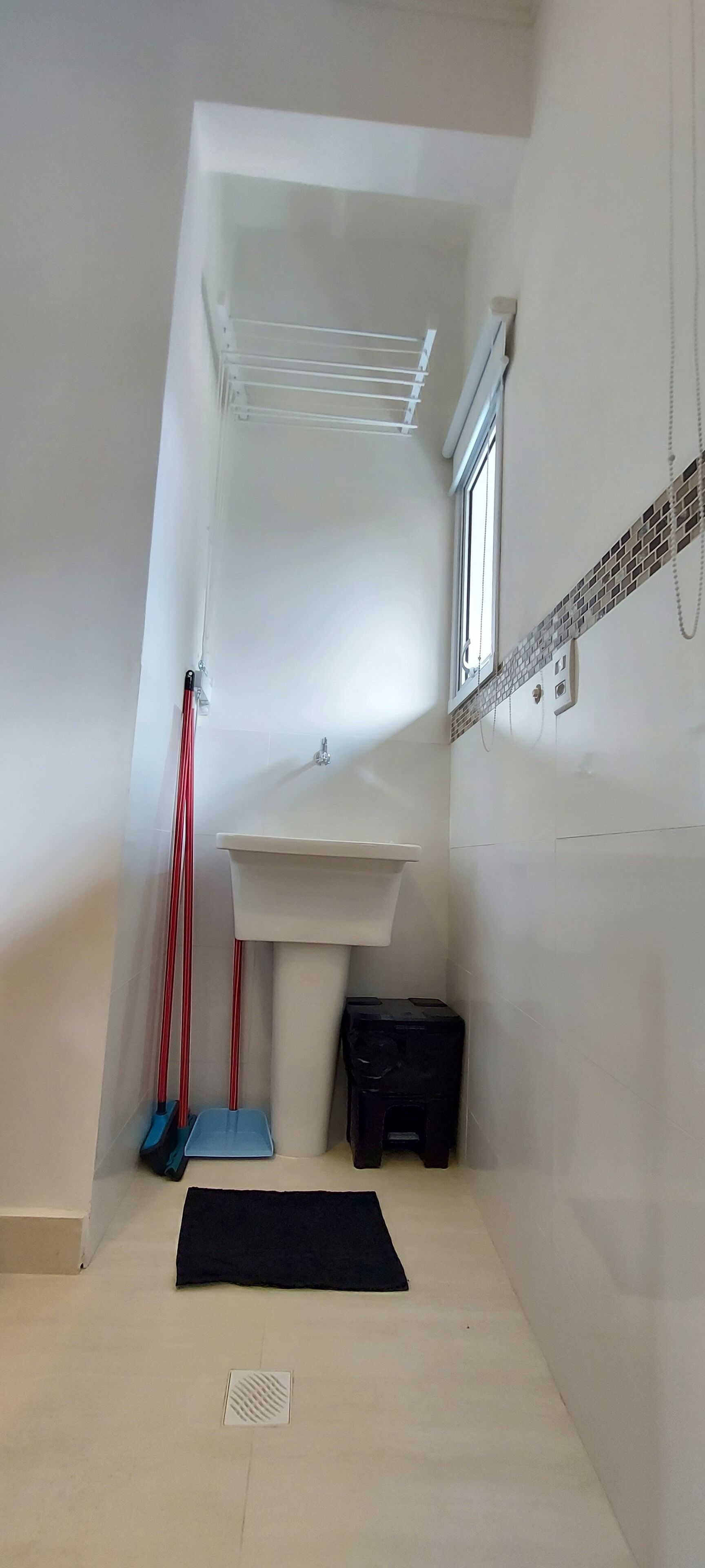 A small, narrow room with a sloped ceiling, a window, a white sink, and a black storage box.
