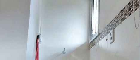 A small, narrow room with a sloped ceiling, a window, a white sink, and a black storage box.