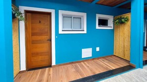 Um corredor com porta de madeira, duas janelas e parede de bambu.