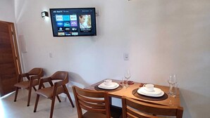 Uma sala de jantar com mesa e cadeiras de madeira, televisão de tela plana na parede e luminária pendente sobre a mesa.