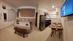Quarto de hotel moderno com cama, mesa de jantar, televisão e área de cozinha.