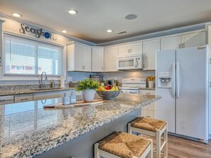 A modern kitchen with white cabinets, granite countertops, and a central island with seating. - "SeaShore Retreat" 5 bed/3 bath home direct Oceanfront on Topsail Island (North Topsail Beach)
