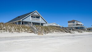 Uma casa à beira-mar com uma varanda saliente, um terraço no segundo andar e uma escadaria que dá para a praia.