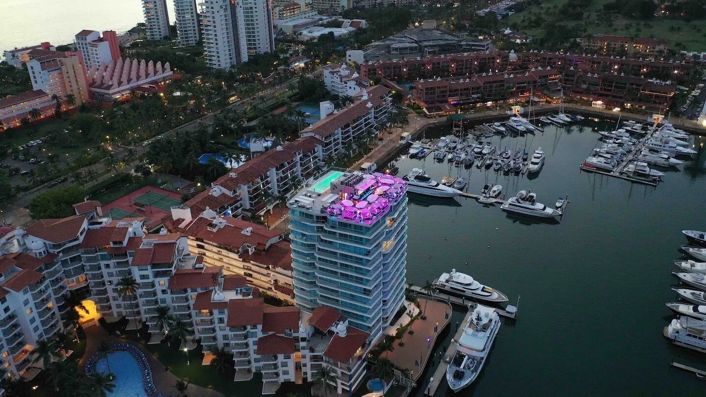 A high-rise hotel with multiple balconies, a marina with boats, and a pool area.