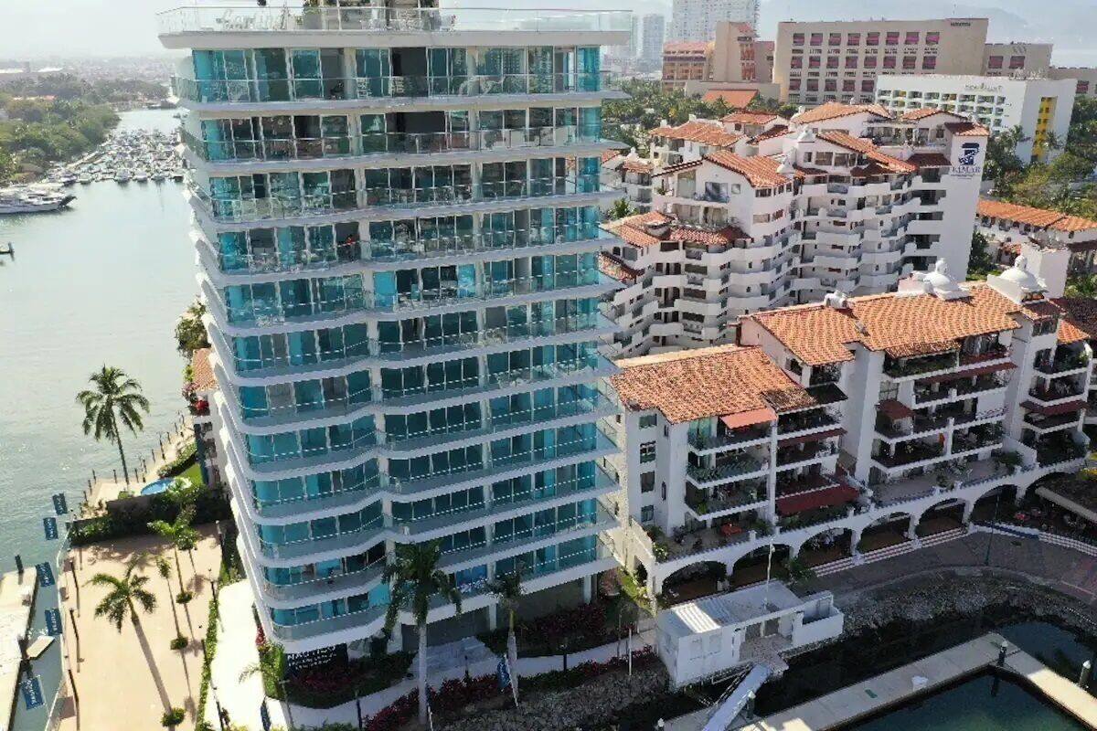 A multi-story hotel with balconies, a pool, and a marina in the background.