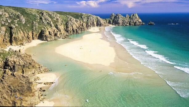 Un paysage côtier caractérisé par une plage de sable, des falaises rocheuses et une eau d’un bleu limpide.
