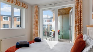 Une chambre d’hôtel avec un grand lit, une vue sur l’extérieur et un balcon équipé d’une table et de chaises.
