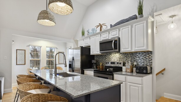 A modern kitchen with white cabinetry, a granite island, and a backsplash with a mosaic tile pattern. - Beach Villa with Private Pool - Walk to beach and Island View Casino (Gulfport)