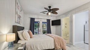 A bedroom with a bed, a ceiling fan, a TV mounted on the wall, and a bathroom visible through an open door. - Beach Villa with Private Pool - Walk to beach and Island View Casino (Gulfport)
