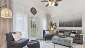 A living room with a grey sofa, a blue armchair, a grey ottoman, a patterned rug, and a ceiling fan. - Beach Villa with Private Pool - Walk to beach and Island View Casino (Gulfport)